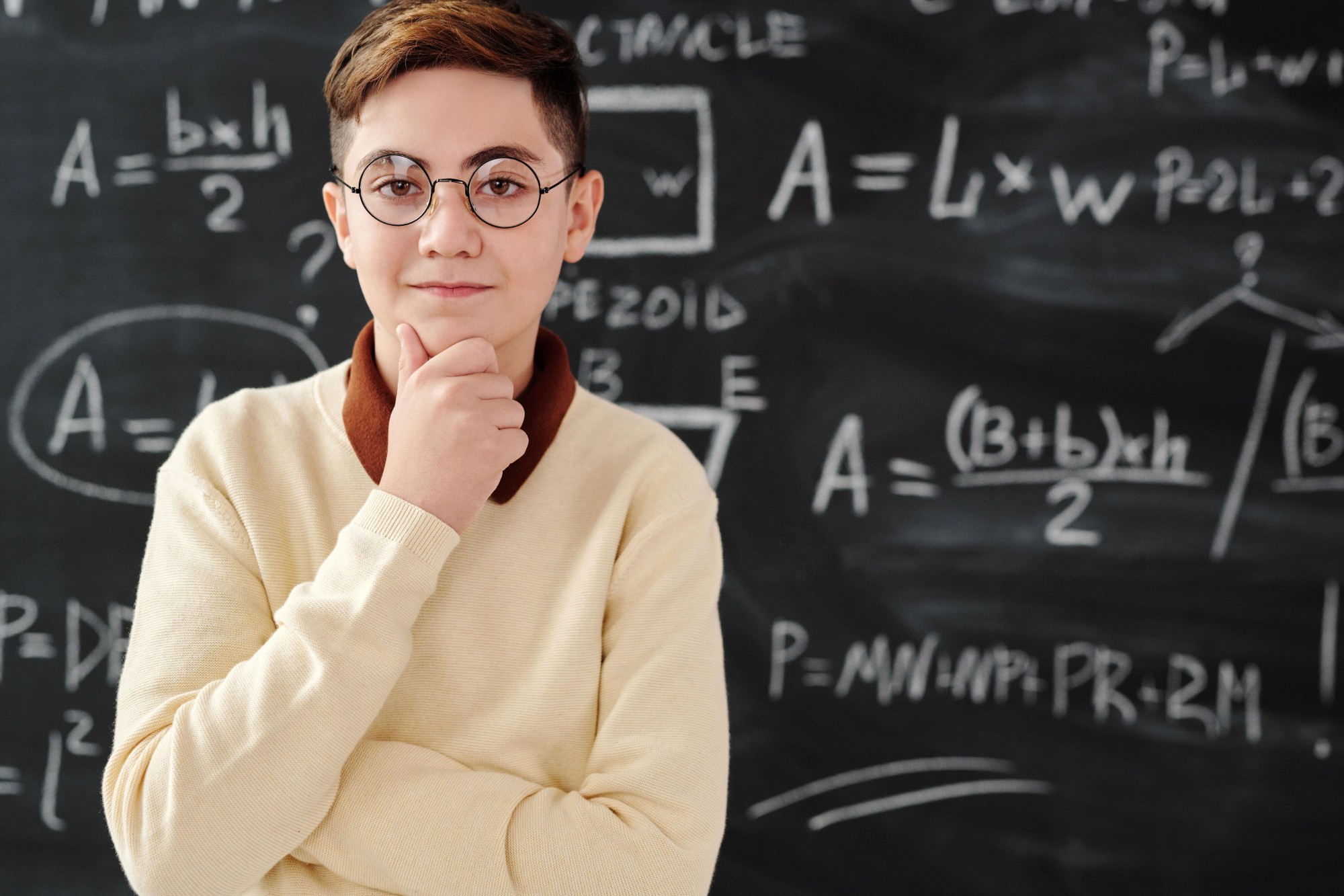 Aluno com óculos, pensativo, diante de um quadro com fórmulas de matemática e geometria